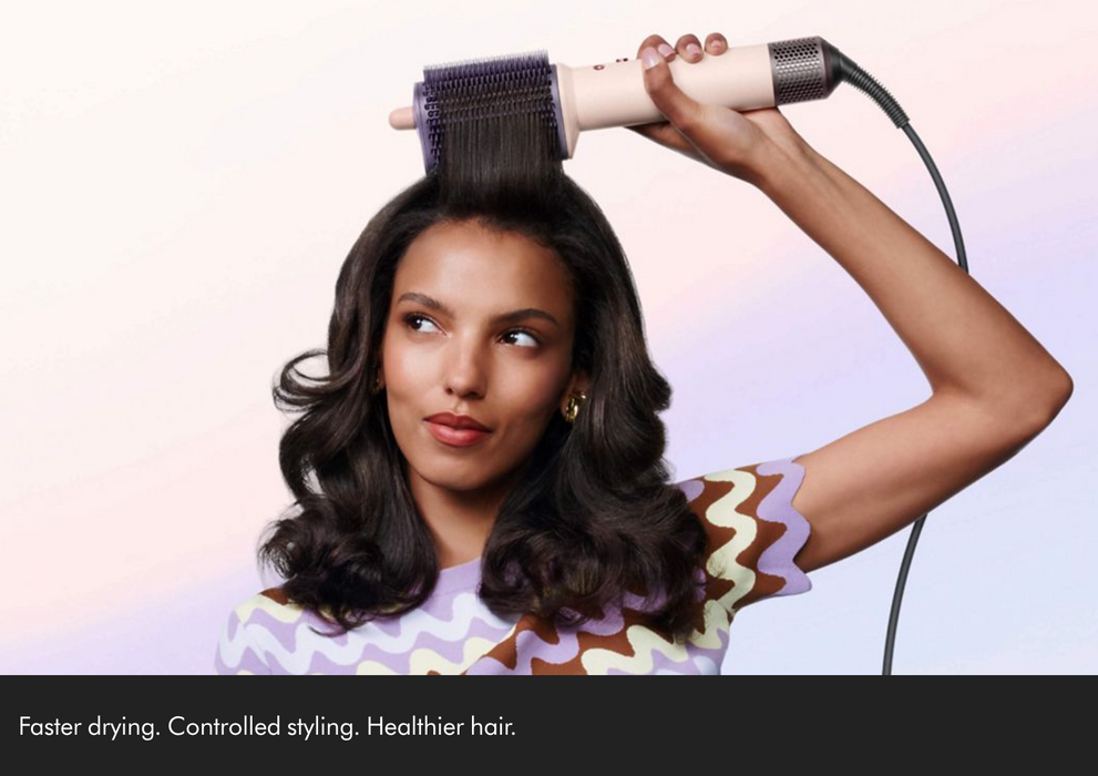 A woman with long dark wavy hair uses a cream-colored round hair dryer with a dark purple bristle barrel on a light pastel background. A black banner at the bottom contains the text 'Faster drying.