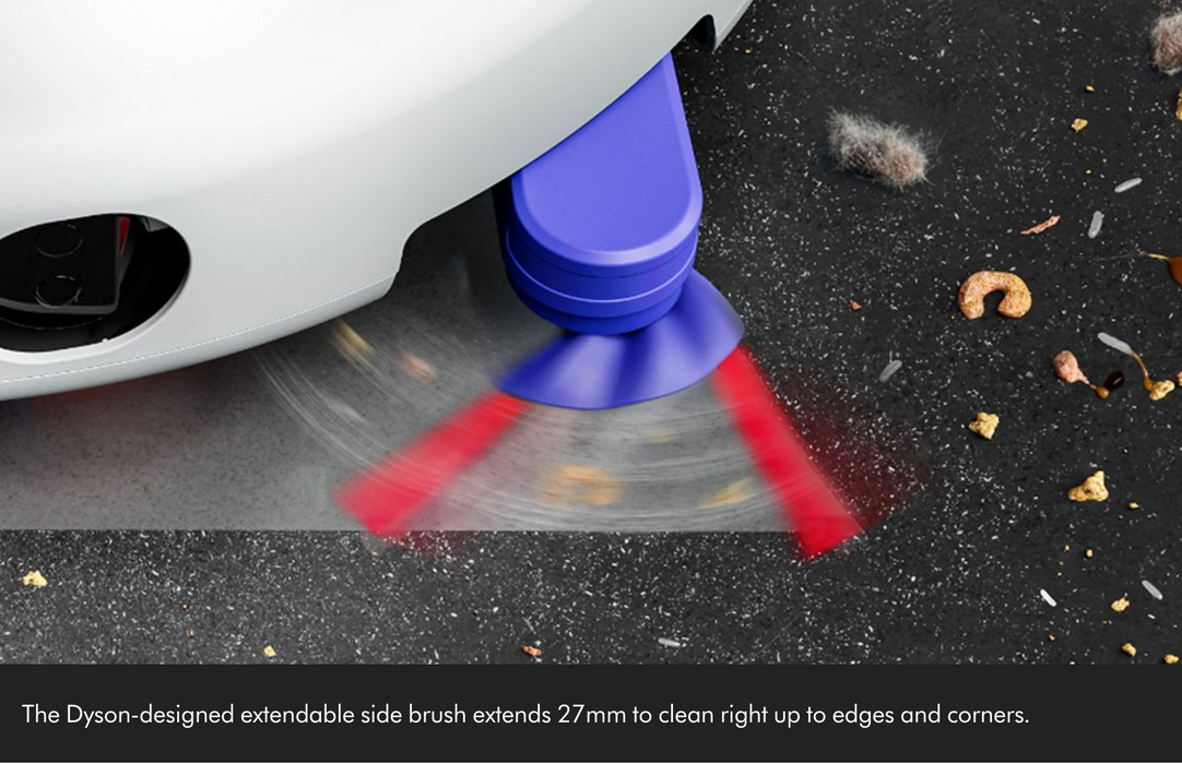 A close-up of a white vehicle underbody using a blue and purple extendable side brush attachment on a dark textured surface, with red motion blur indicating rotation. Small debris is visible on the surface, and a text overlay at the bottom describes the brush extension.
