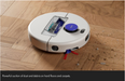 A white robotic vacuum cleaner with a blue power button is shown on a wooden floor, picking up dust and debris. A black banner at the bottom contains descriptive text.