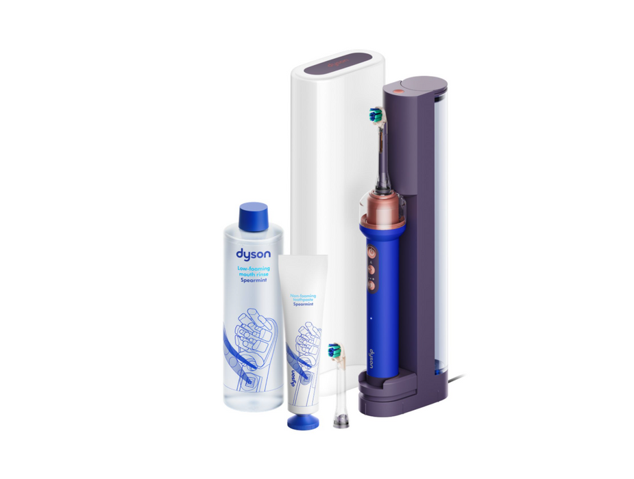 Dyson oral care product set on a white background, including an electric toothbrush with a charging dock, a bottle of oral irrigator cleaner, a tube of toothpaste, and replacement heads.