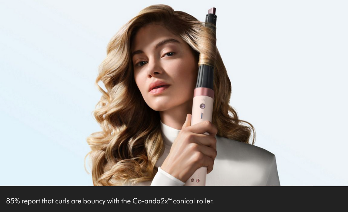 A woman with long wavy blonde hair holds a Co-anda 2x conical roller curling iron against her hair. She is wearing a white top, set against a light blue background with a black banner at the bottom containing a marketing quote.