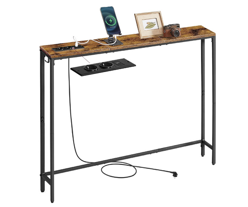 A rustic industrial console table with a weathered brown wood top and black metal legs, featuring a built-in black power outlet panel on the front. The table is shown styled with a smartphone on a charging dock, a picture frame, a camera, and other accessories against a solid white background.