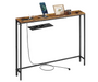 A rustic industrial console table with a weathered brown wood top and black metal legs, featuring a built-in black power outlet panel on the front. The table is shown styled with a smartphone on a charging dock, a picture frame, a camera, and other accessories against a solid white background.