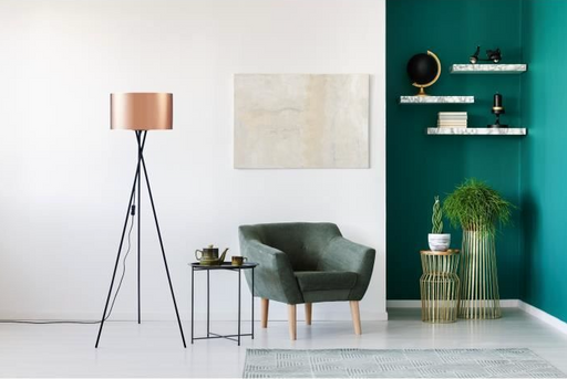 Copper floor lamp with Black metal feet in living room with green armchair and green feature wall